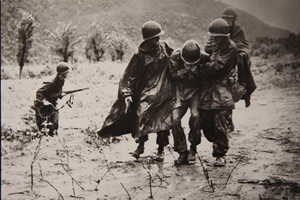 One of the two iconic photographs of Father Emil Kapaun shows him and another soldier carrying an exhausted GI off a battlefield in Korean, early in the war. The photo shows Kapaun to the GI's left. The soldier on the GI's right side was Capt. Jerome A. Dolan, a medical officer with the 8th Cavalry regiment.